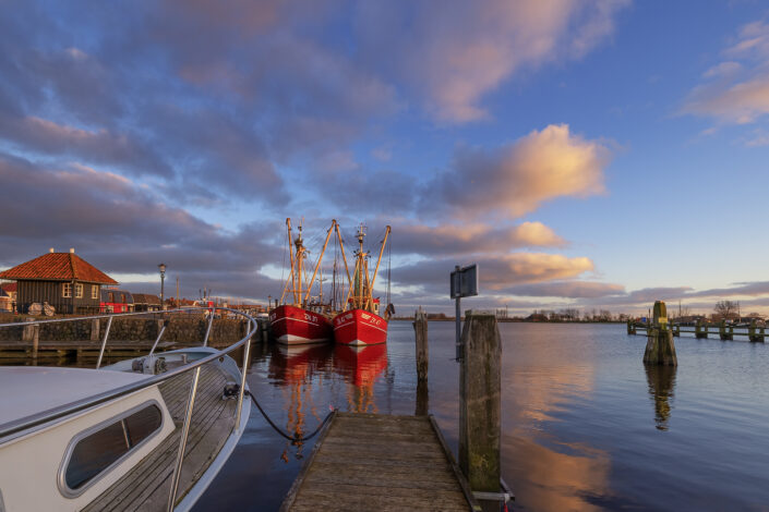 Het laatste licht valt op de haven van Zoutkamp tijdens de zonsondergang. Het mooie heldere winterlicht zorgt voor diepe blauwe kleuren in de lucht die mooi contrasteren met de rode kleuren van de vissersschepen.