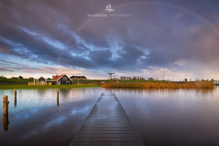 Een mooie regenboog tijdens de zonsopkomst boven het Lauwersmeer in Friesland. In de lucht drijven mooie wolken voorbij.