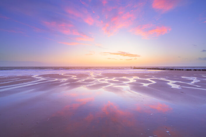 Een lucht vol avondrood reflecteert op het natte zand van het strand van Zoutelande tijdens een rustgevende zonsondergang.