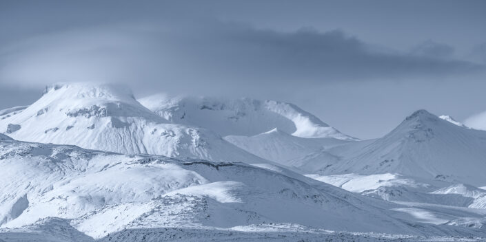 Besneeuwd berglandschap in de hooglanden op IJsland met de toppen van de bergen in de wolken.