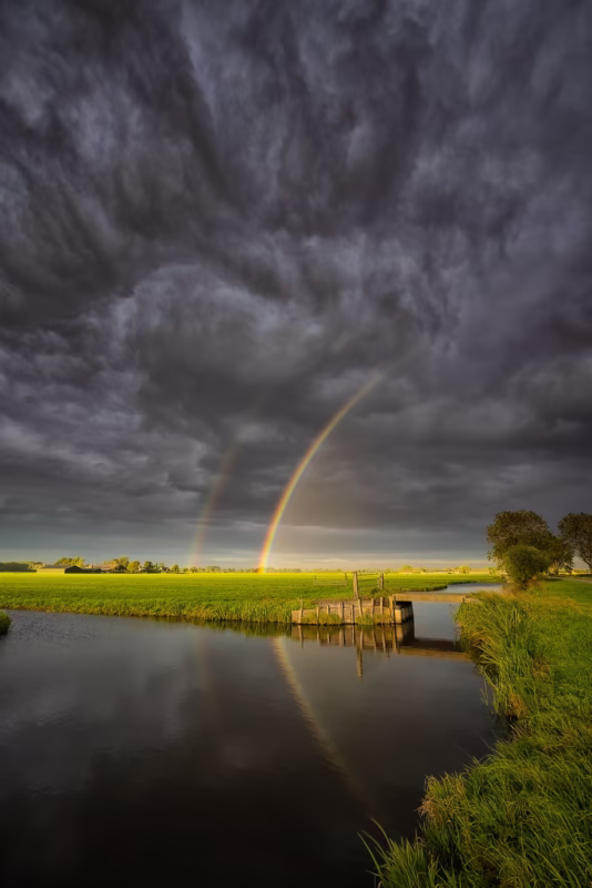 Donkere onweerswolken met een regenboog boven de polders bij Overslingeland