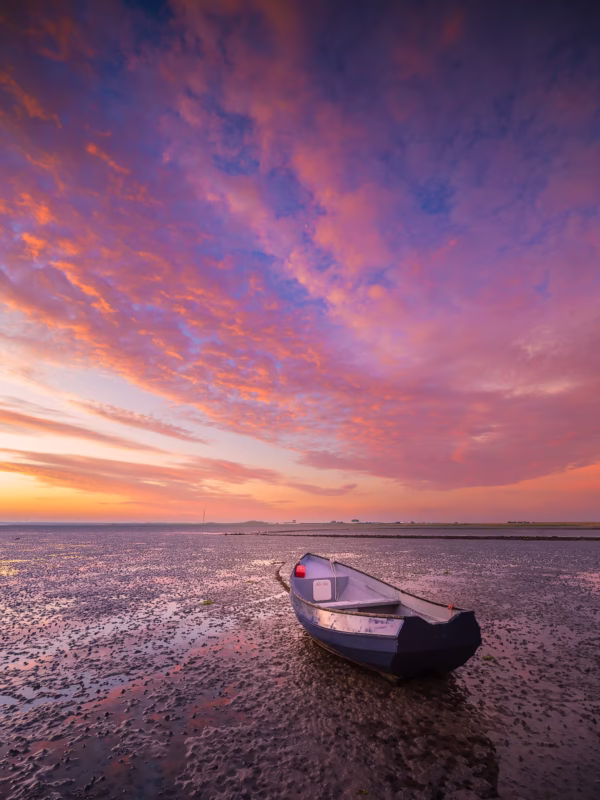 Een drooggevallen bootje in de Oosterschelde in Zeeland met een zonsopkomst met ochtendrood