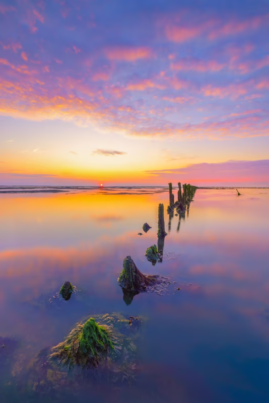 Een oude palenrij in de Waddenzee met een mooie zonsondergang met avondrood