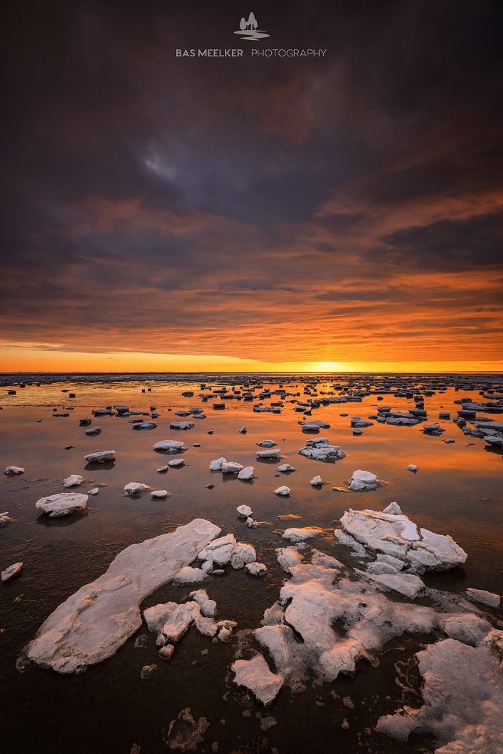 De Waddenzee is bedekt met IJsschotsen in de winter. Een mooie zonsondergang geeft prachtige kleuren in de lucht en de laatste zonnestralen geven het landschap een warme gloed.