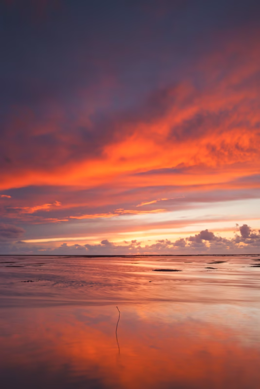 De wolkenlucht tijdens de zonsondergang reflecteert op het water va de Waddenzee