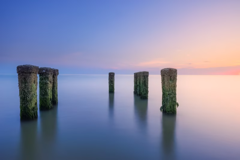 Palen in het water in zee op het strand van Westkapelle tijdens de zonsondergang