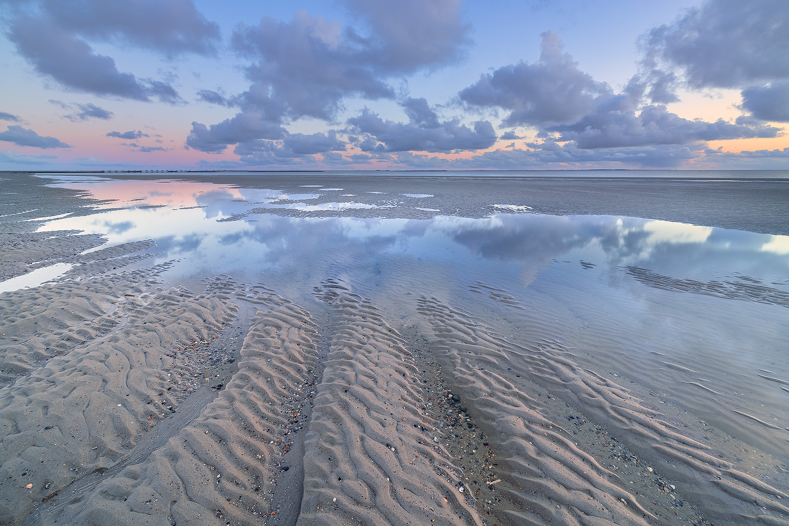 Eb op het strand van Westerschouwen op Schouwen-Duivenland in Zeeland. De wolken weerspiegelen in het water op het strand tijdens zonsondergang.