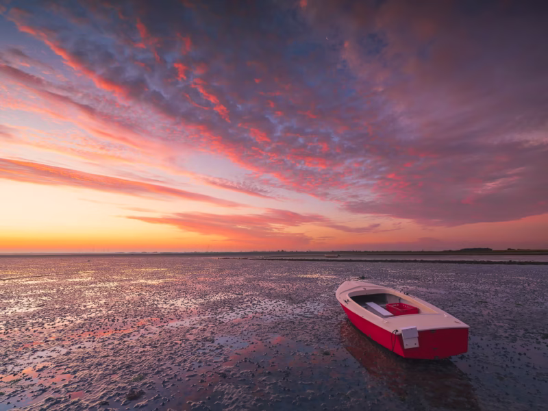 Een drooggevallen bootje op de Oosterschelde met een spectaculaire zonsopkomst